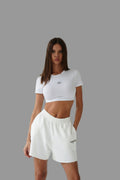 Woman wearing a white crop top and shorts on a gray background